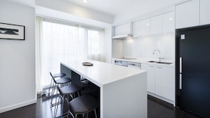 Una cocina moderna con una isla central, taburetes de bar, un refrigerador negro y muebles de cocina blancos.