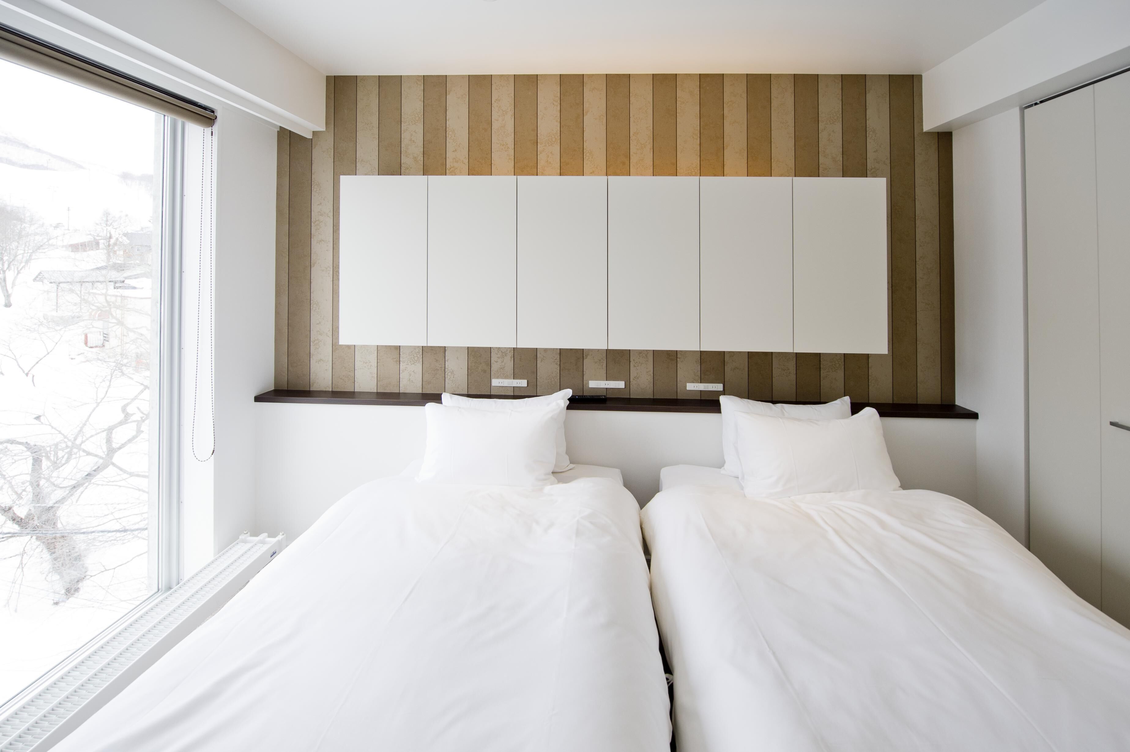 Een moderne slaapkamer met twee bedden, een groot raam en een inbouwkast.