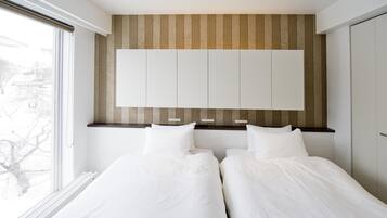 Een moderne slaapkamer met twee bedden, een groot raam en een inbouwkast.