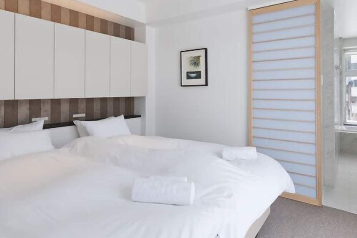 A modern hotel room with a large bed, built-in wardrobe, and a sliding door.