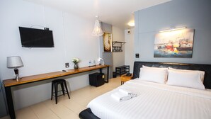 A hotel room with a bed, a desk with a chair, a TV, a painting, and a lamp. - Phusuang Place (Chiang Mai)