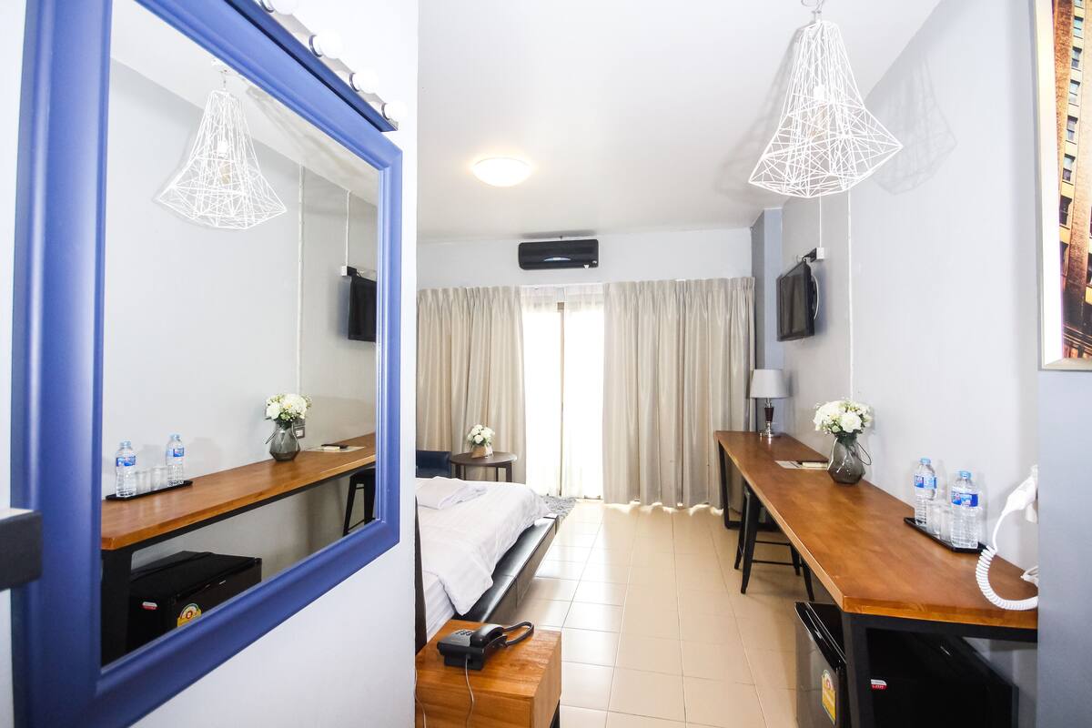 A hotel room with a bed, a desk, a mirror, a TV, and a window with curtains.
