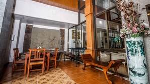 A lobby with a wooden bench, a table, and chairs. There is a large window with a view of the outside. - Phusuang Place (Chiang Mai)