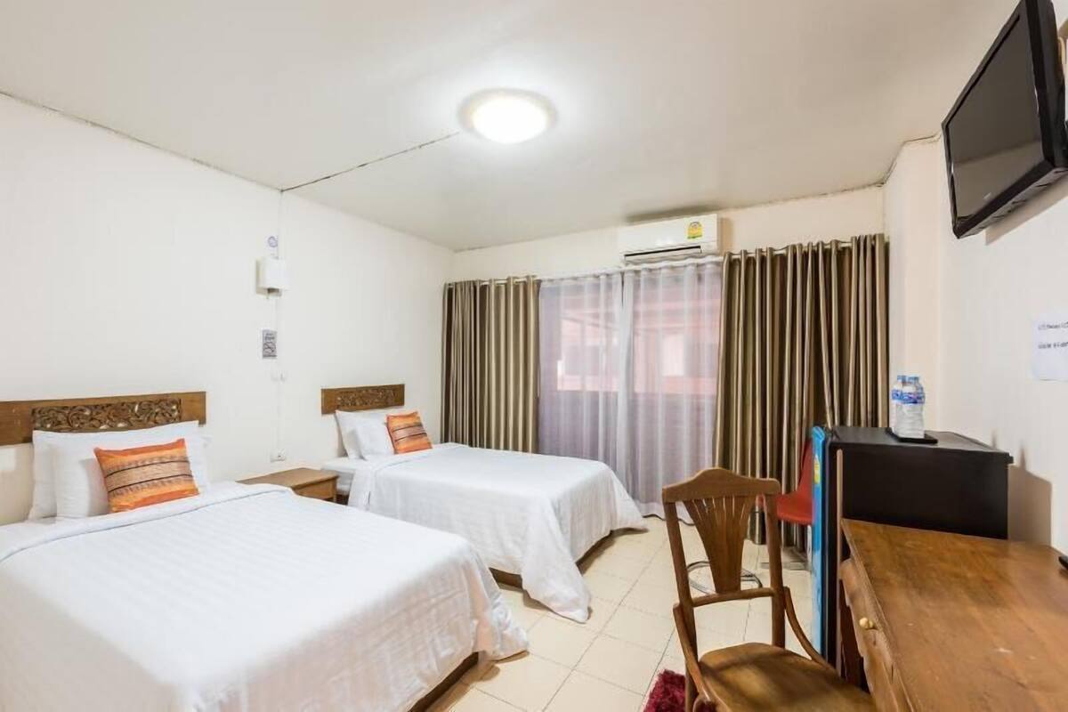 A hotel room with two beds, a desk, a chair, a television, and an air conditioning unit.
