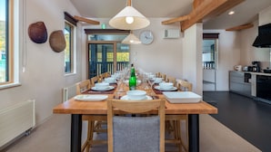 A dining area with a long wooden table set for a meal, surrounded by chairs, with a hanging light fixture above. - Gondola Chalets (Kutchan)