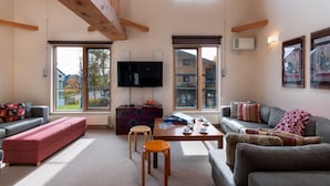 A spacious living room with a large TV, wooden beams, and large windows offering views of the outside. - Gondola Chalets (Kutchan)