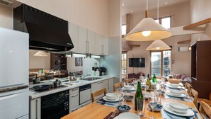 A modern kitchen with white cabinets, a black range hood, and a dining area set for a meal with plates, bowls, and glasses. - Gondola Chalets (Kutchan)