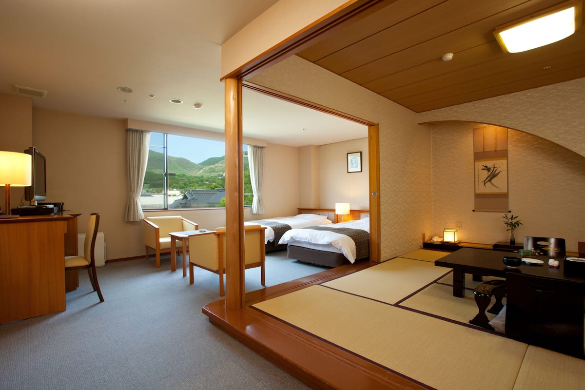 Quarto de hotel com cama, secretária, cadeira e vista para o exterior.