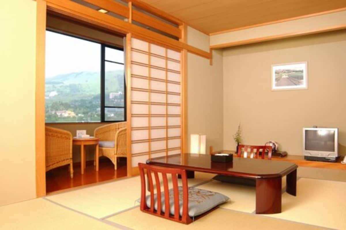Um quarto tradicional japonês com piso de tatame, uma mesa de madeira baixa e uma televisão.