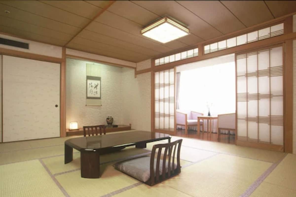 Um quarto japonês tradicional com tatames, uma mesa baixa, almofadas, portas deslizantes e um quadro na parede.