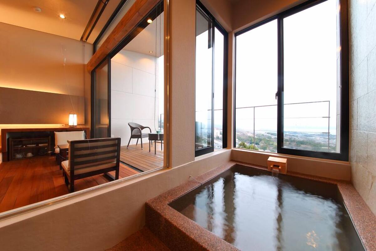A modern room with a hot tub, large windows, a wooden floor, and a view of the city.