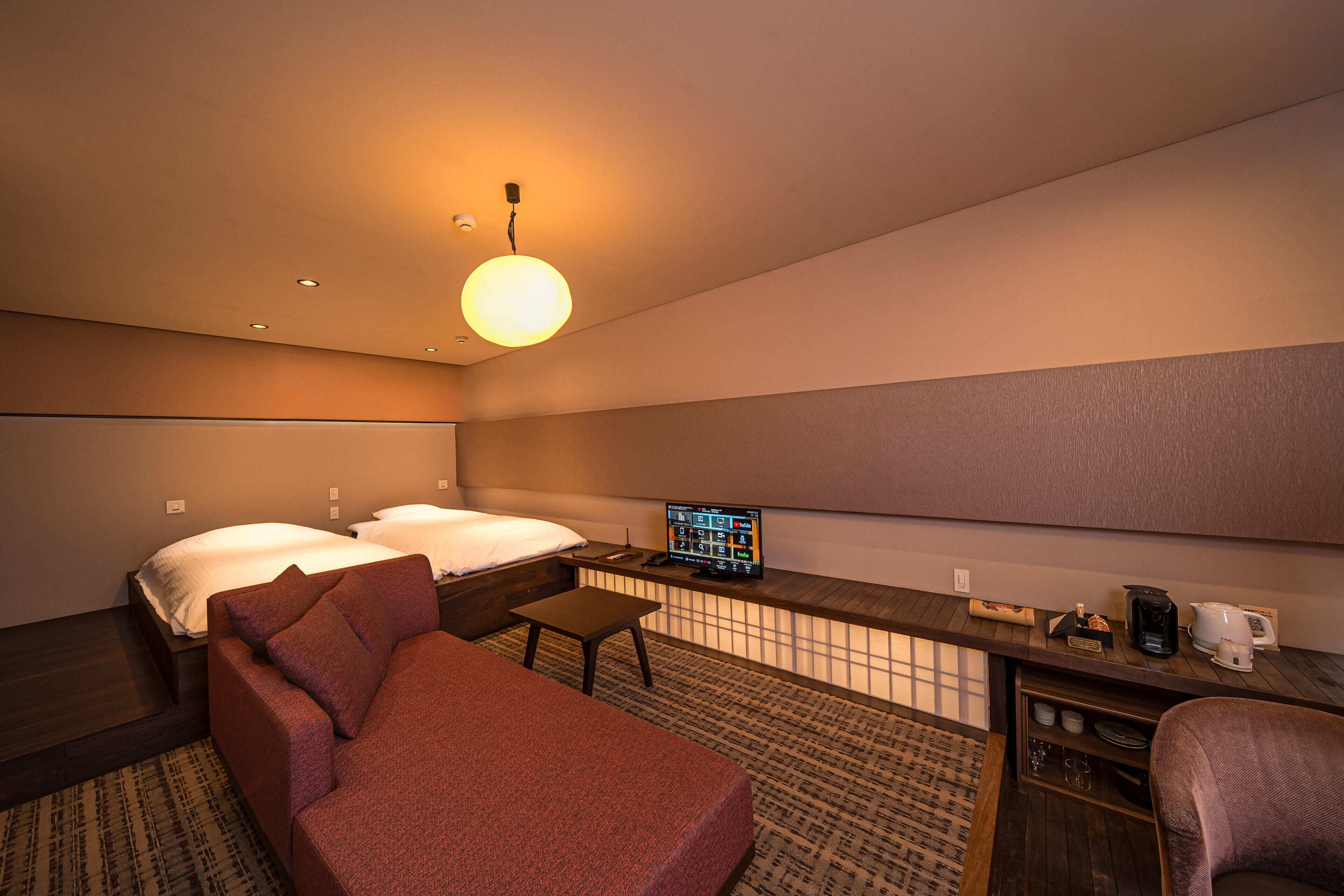 Habitación de hotel con cama, sofá, una mesita, televisor y cafetera.