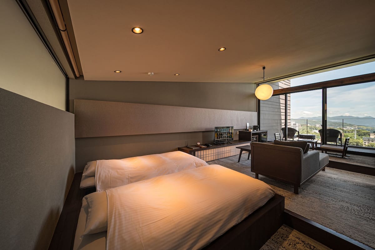 A modern hotel room with a large bed, a desk, a chair, and a view of the city.