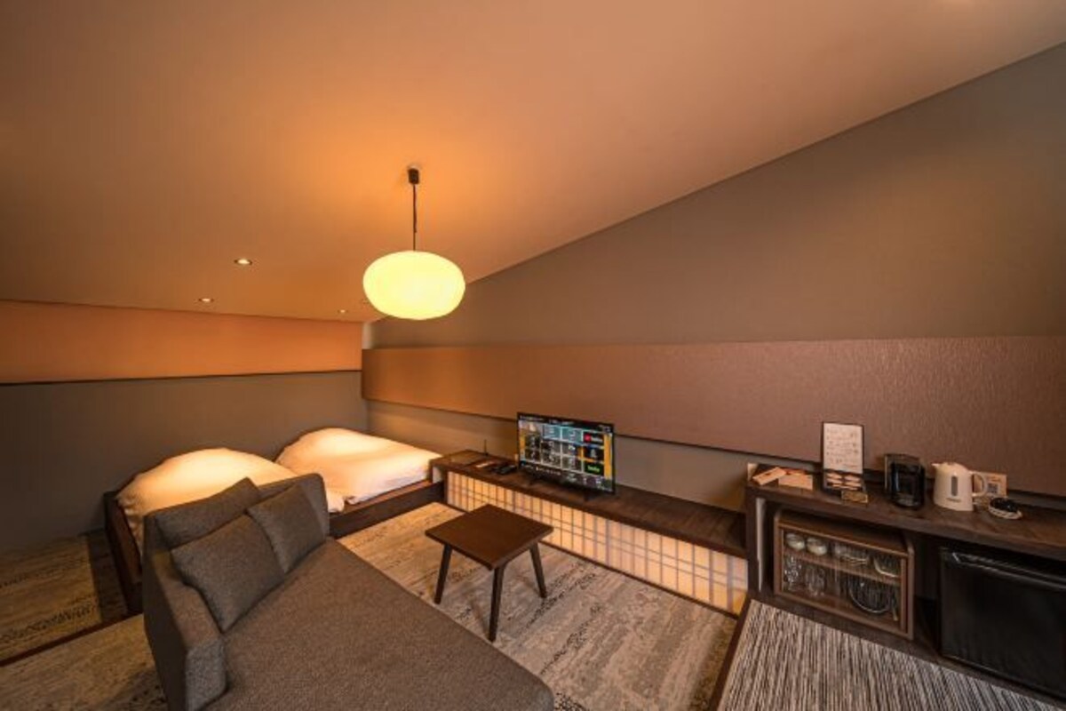 Moderni hotellihuone, jossa on sohva, pieni pöytä, televisio ja minibaari.