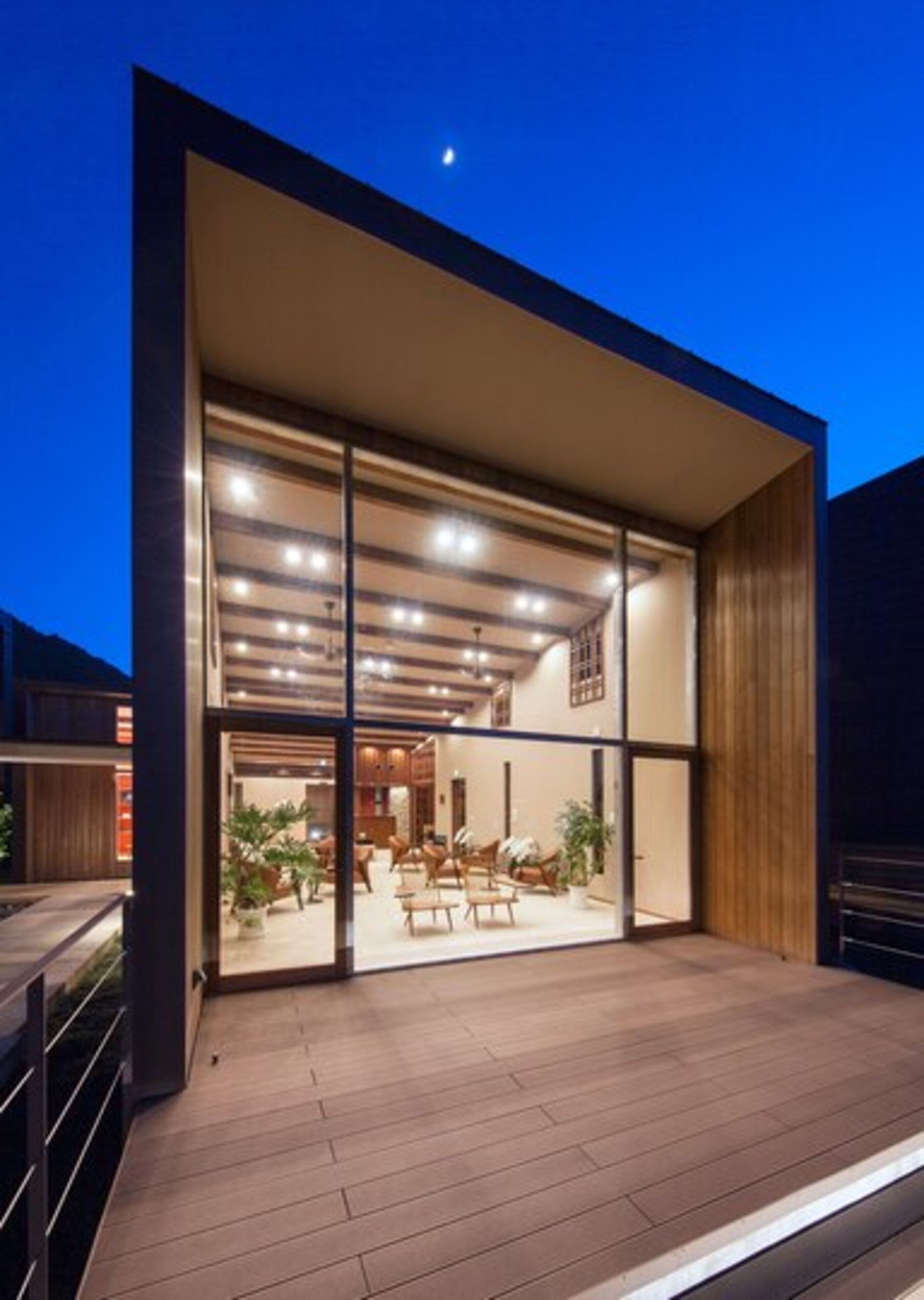 A modern building with a large glass entrance, wooden flooring, and a visible interior with seating and plants.