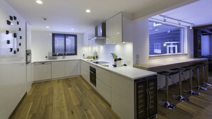 A modern kitchen with white cabinets, a wooden floor, a large window, and a bar area with stools.