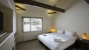 A bedroom with a bed, a bedside table with a lamp, a window, and a radiator.