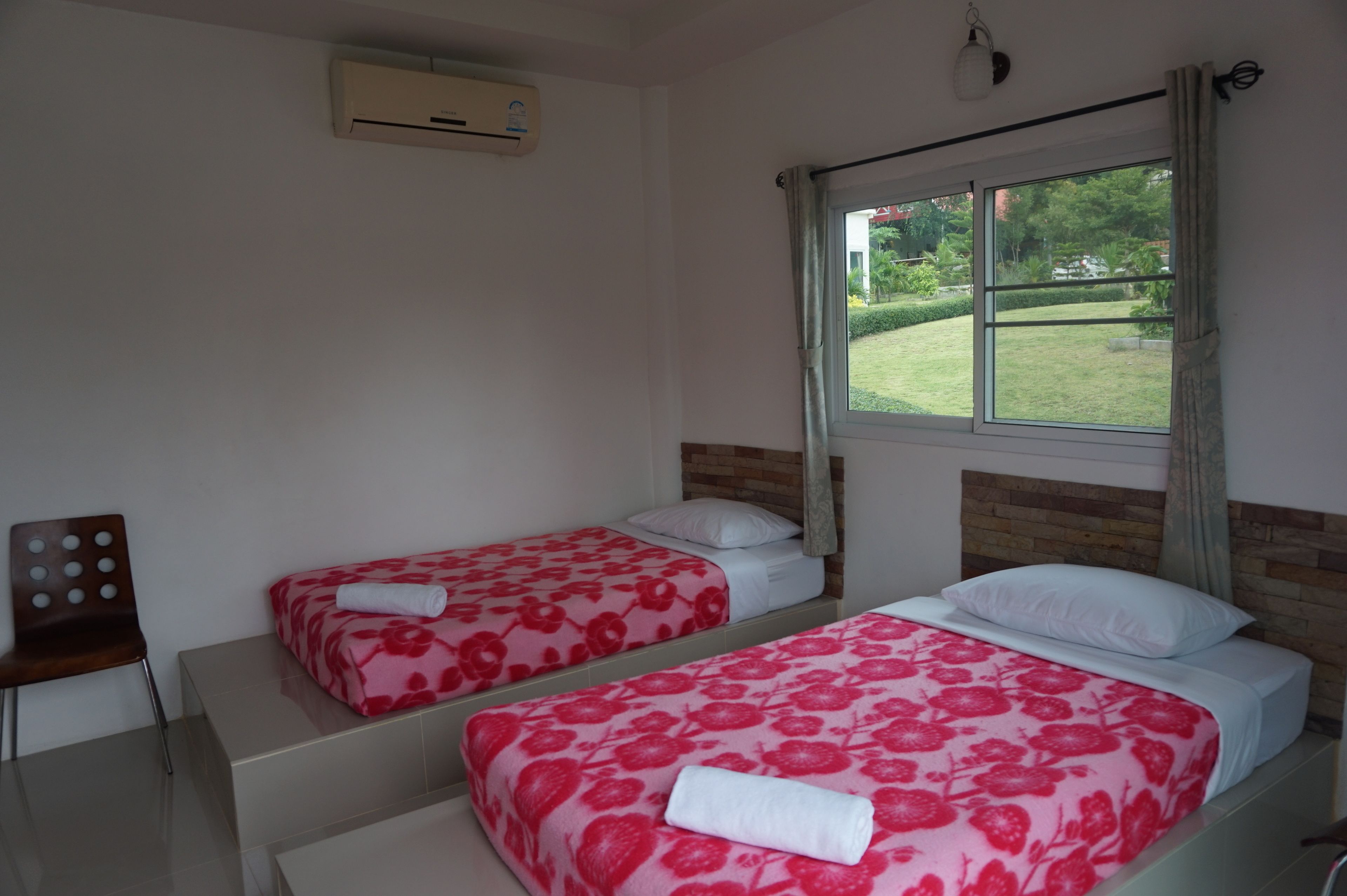 Habitación de hotel con dos camas, una ventana con vista a un jardín, cabecera de madera y una silla.