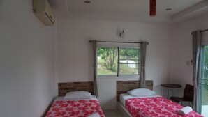A hotel room with two beds, a window with a view of greenery, a small table, and a chair. - WhiteRock Resort Pakchong (Pak Chong)