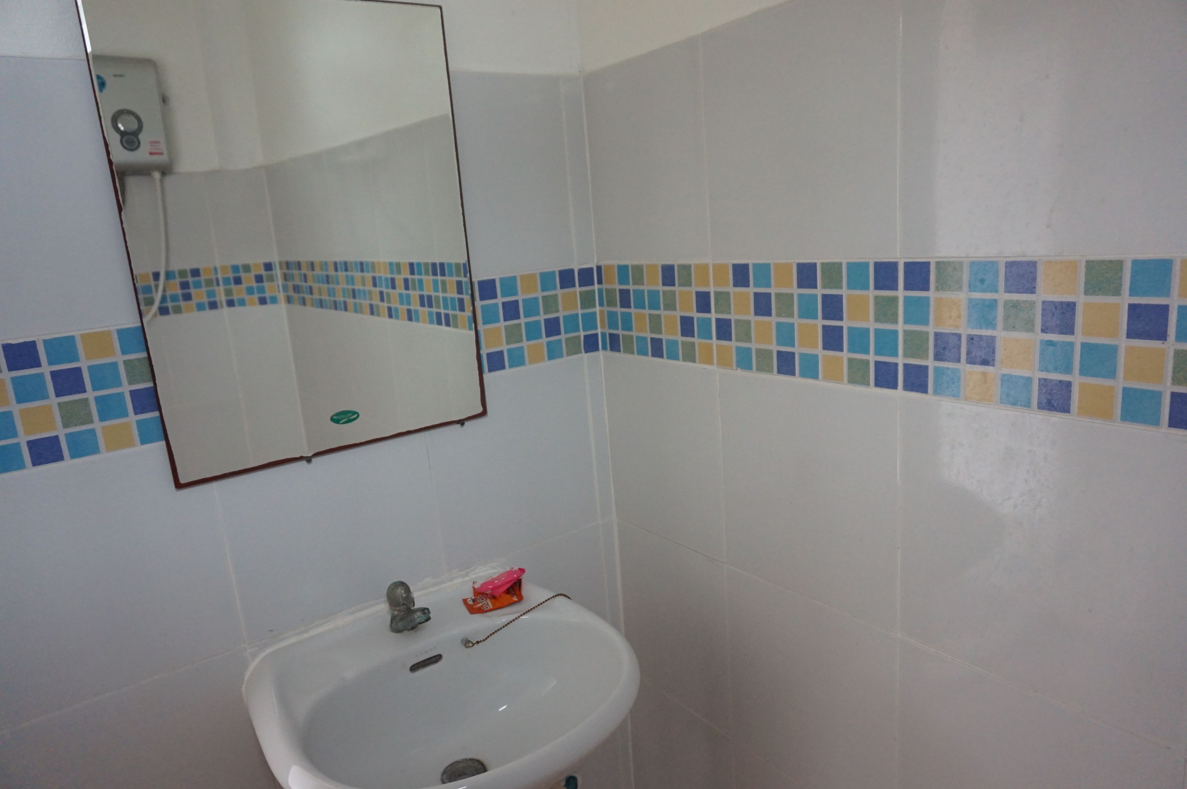 Un baño con lavamanos blanco, espejo y pared de azulejos con detalles azules y amarillos.