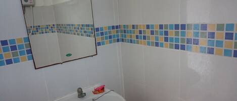 Un baño con lavamanos blanco, espejo y pared de azulejos con detalles azules y amarillos.