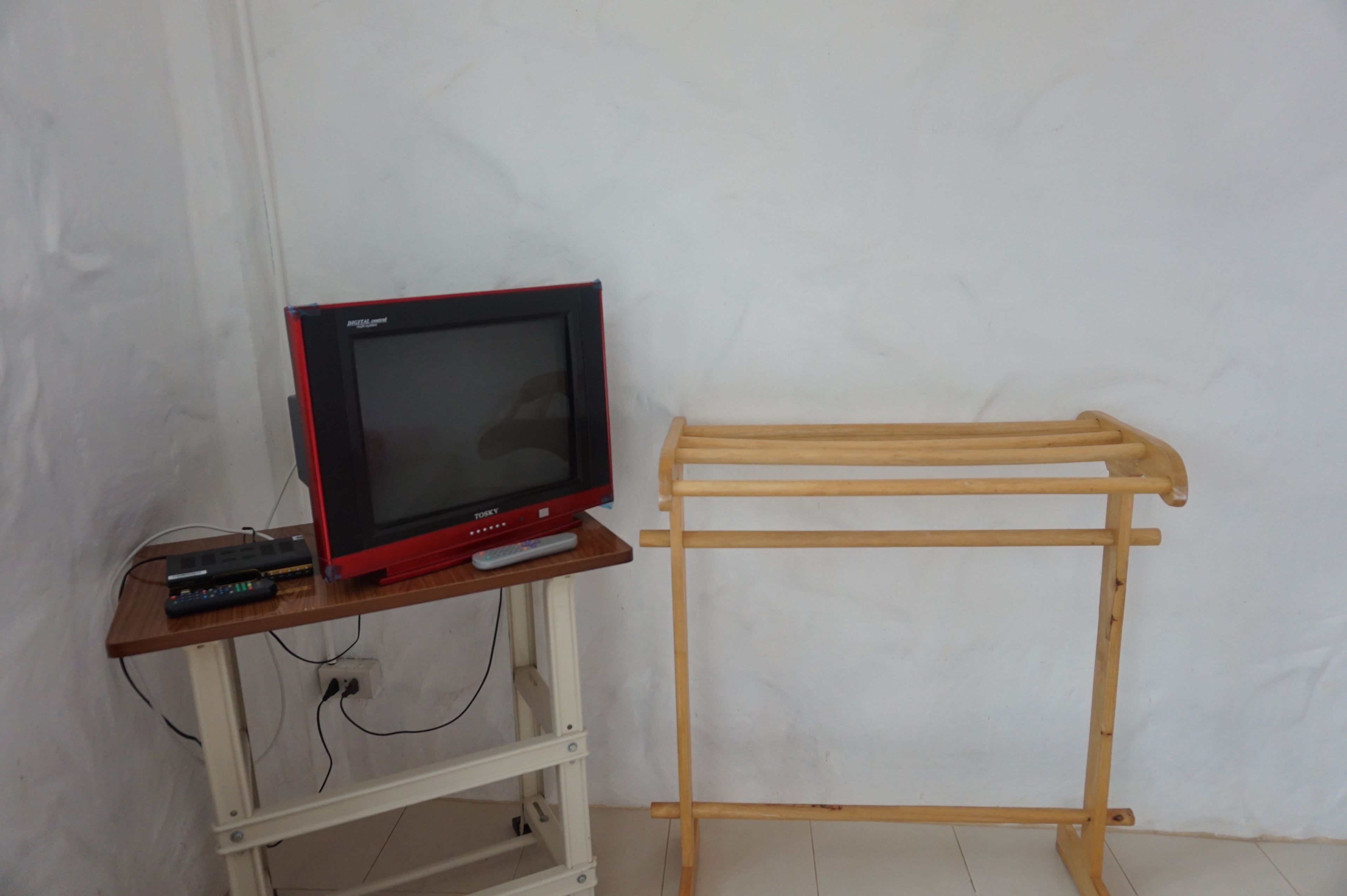 Een televisie op een houten standaard, met een afstandsbediening, aangesloten op een witte muur.