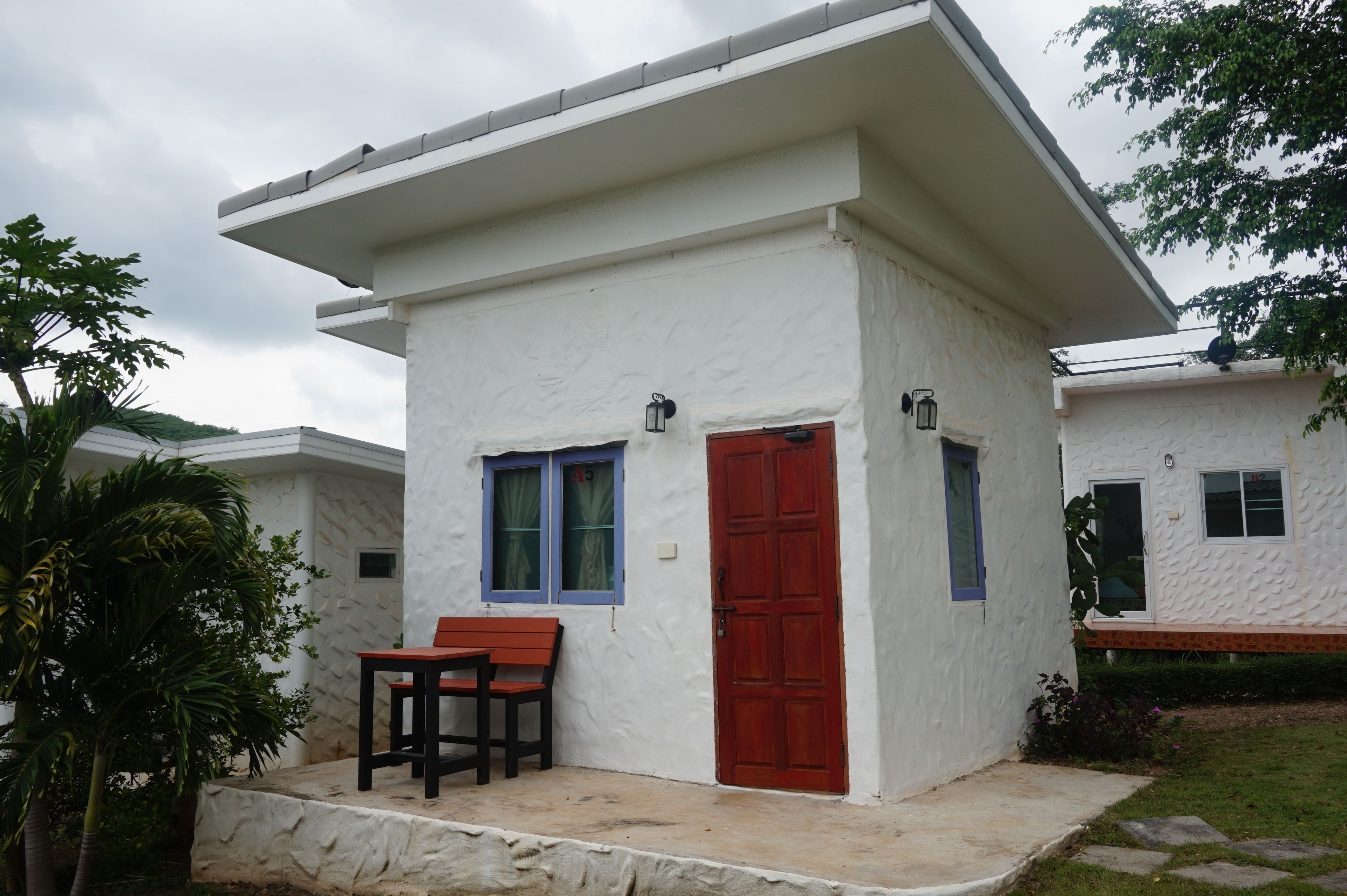 Un edificio blanco con puerta roja, un banco y una pequeña mesa.