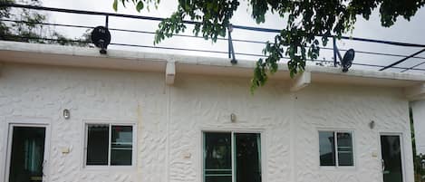 A building with textured white walls, three windows, and a red-tiled base.