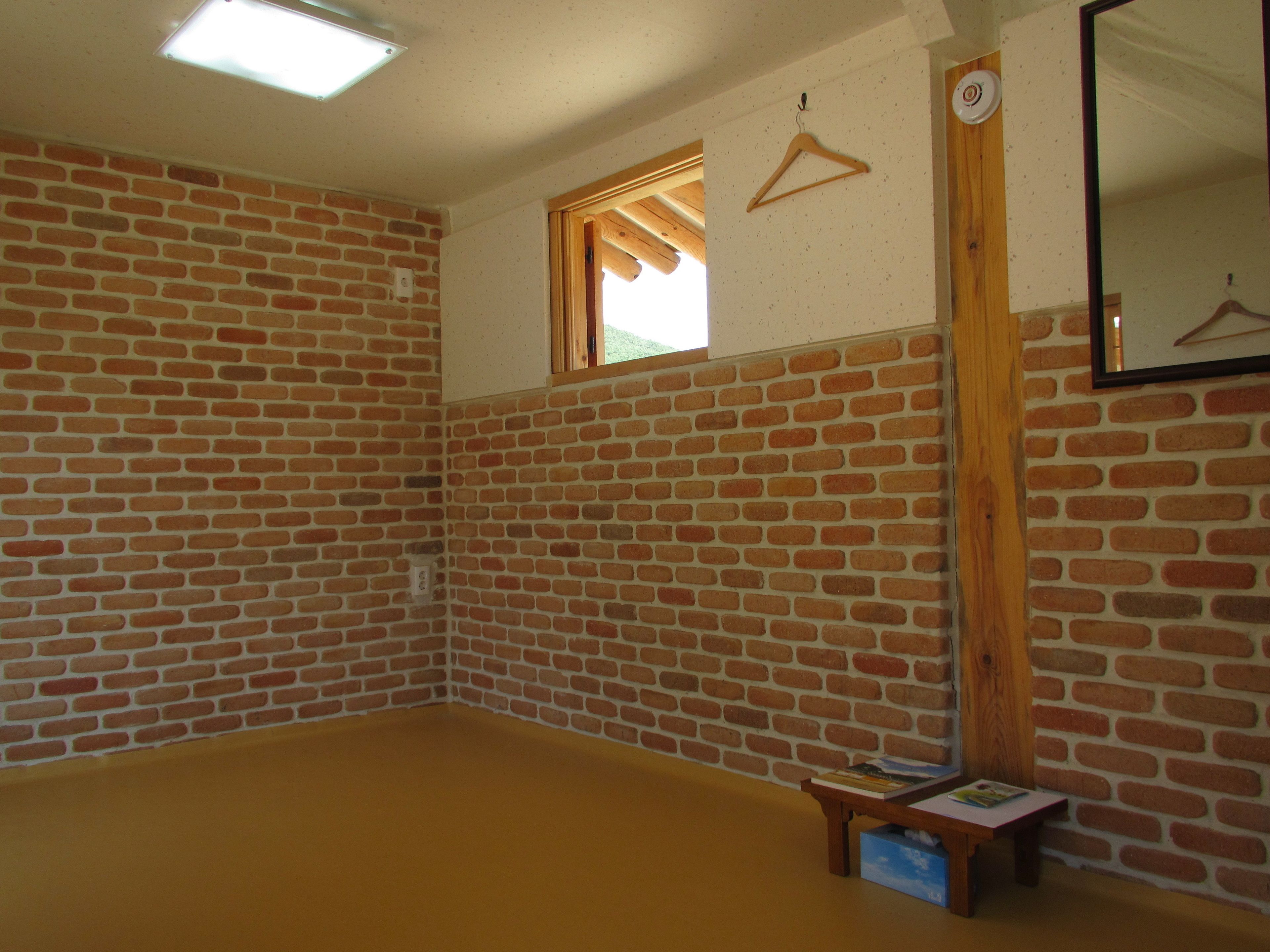 Una habitación con paredes de ladrillo, suelo de madera, una ventana, un espejo y una pequeña mesa con libros.