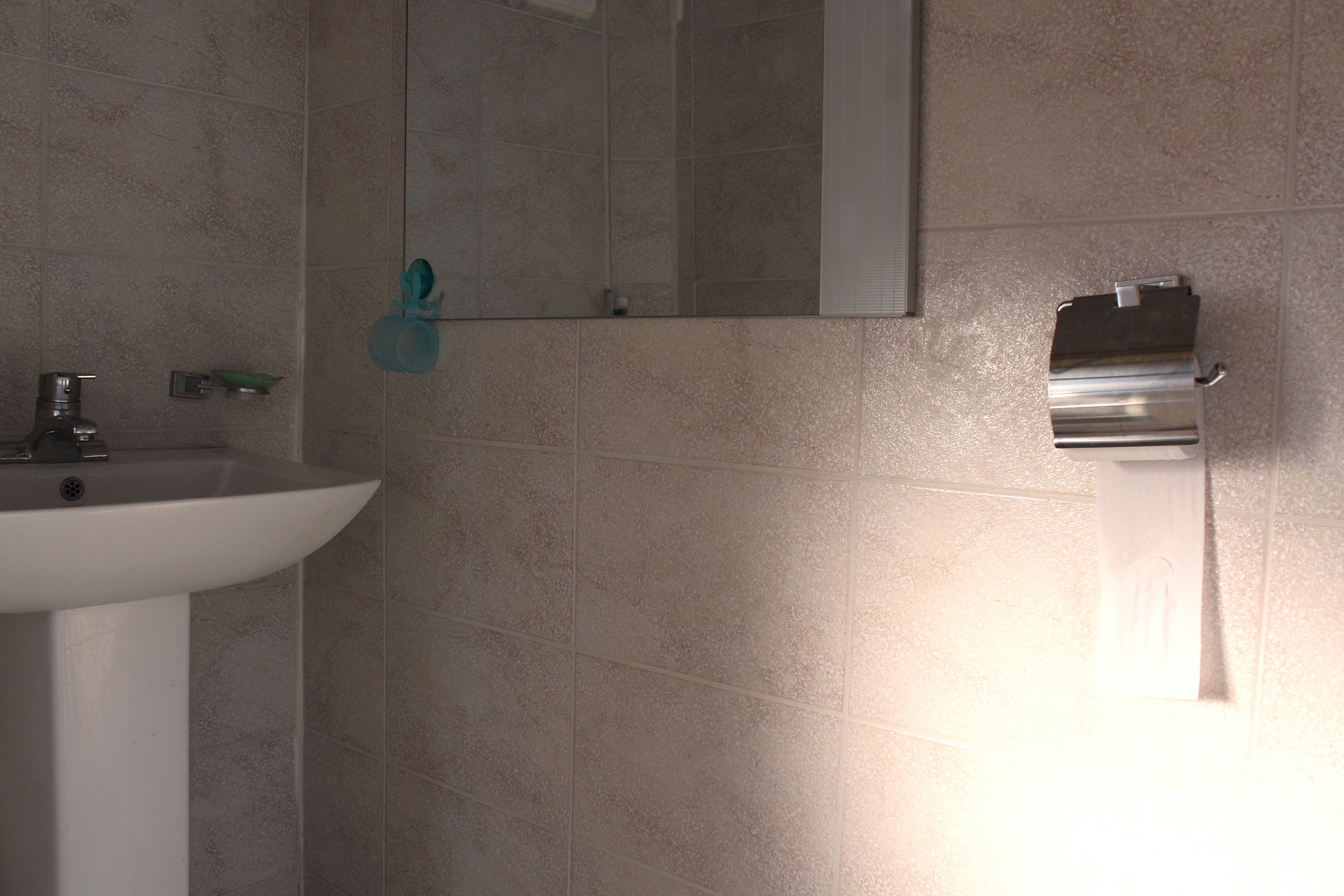 Un baño con lavamanos blanco, un espejo y un dispensador de toallas.