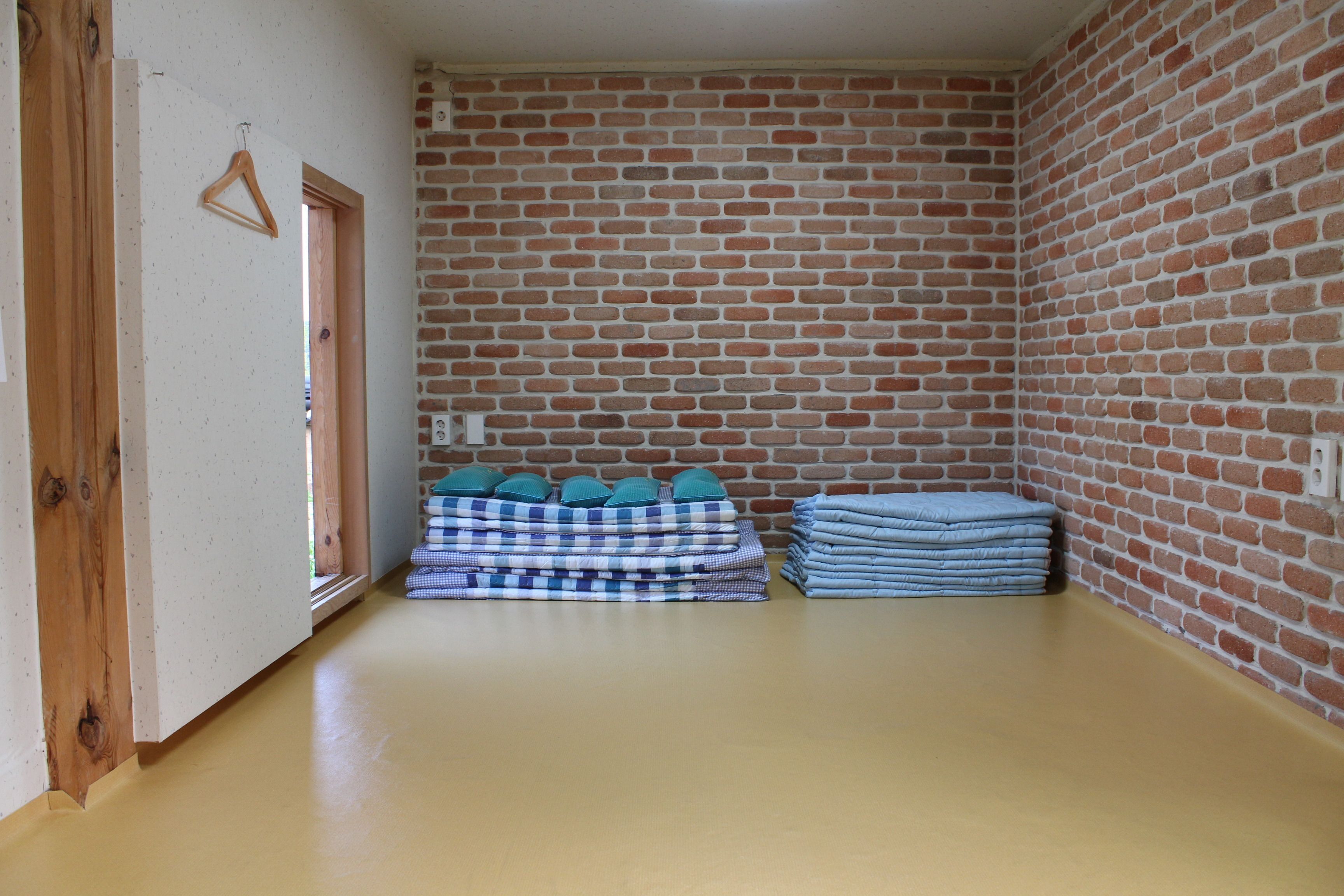 Una habitación con pared de ladrillo, puerta de madera y suelo color beige.