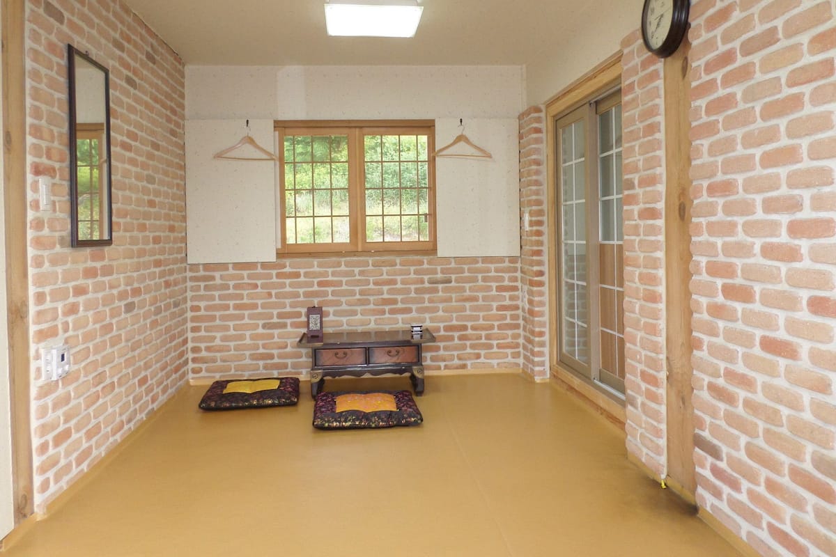 A room with brick walls, a wooden dresser, two padded mats, a hanging clothes rack, and a clock on the wall.