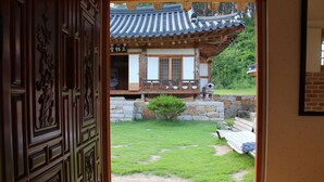 Un edificio coreano tradicional con una puerta de madera, un muro de piedra y un pequeño jardín con un banco y un árbol.