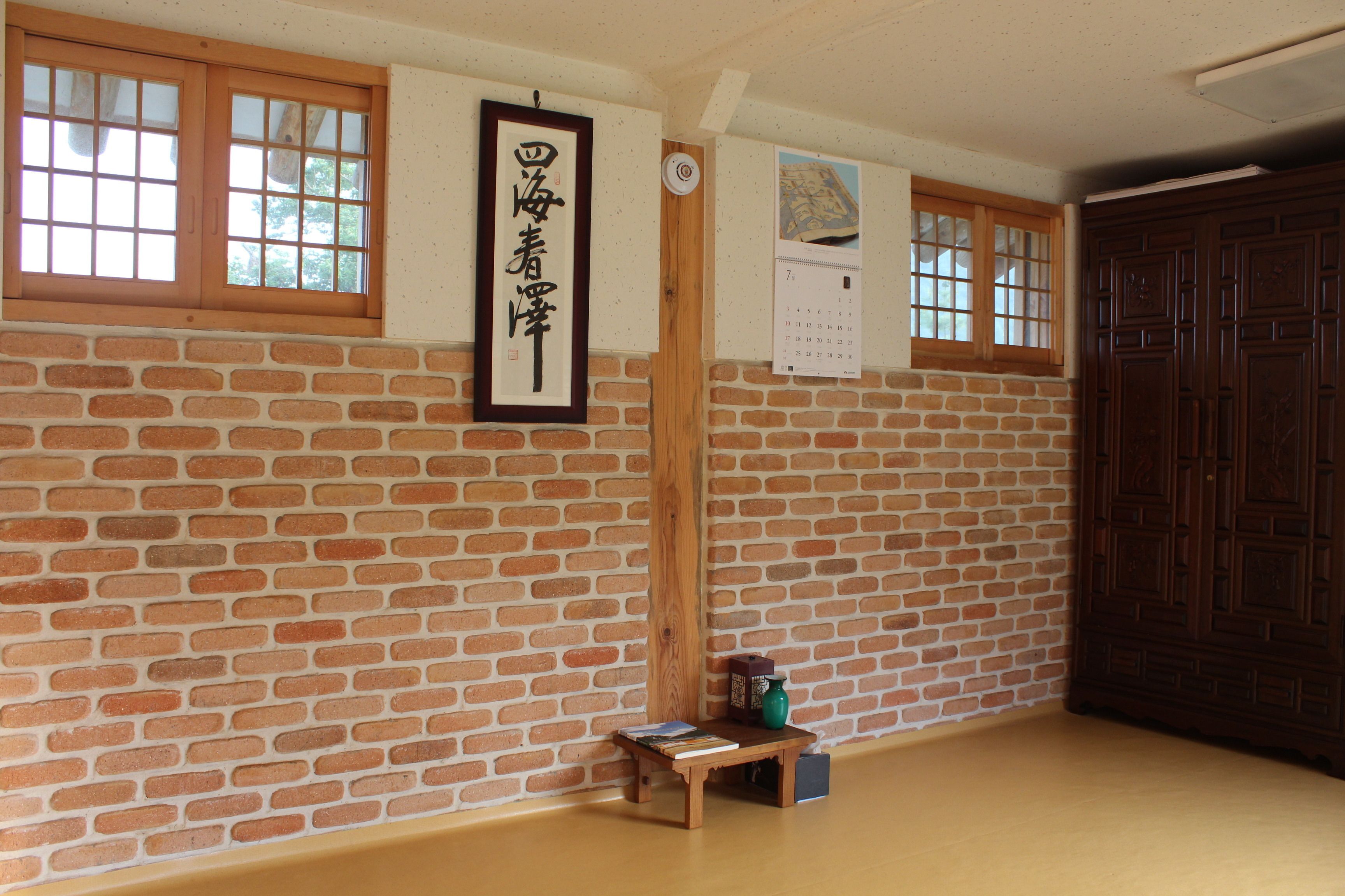 Una habitación con pared de ladrillo, puerta de madera y una pequeña mesa de madera con libros y un florero.