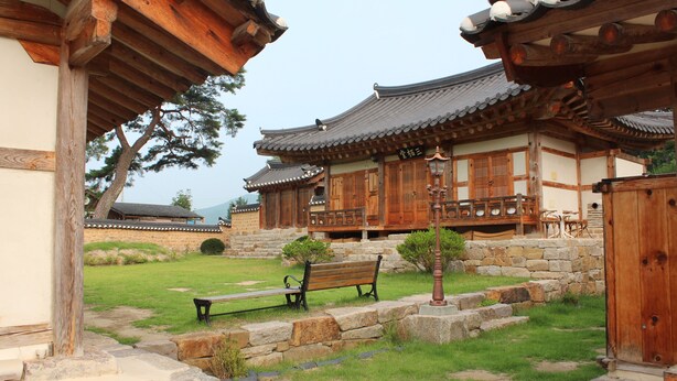Un edificio tradicional coreano con arquitectura de madera, un camino de piedra y un banco.