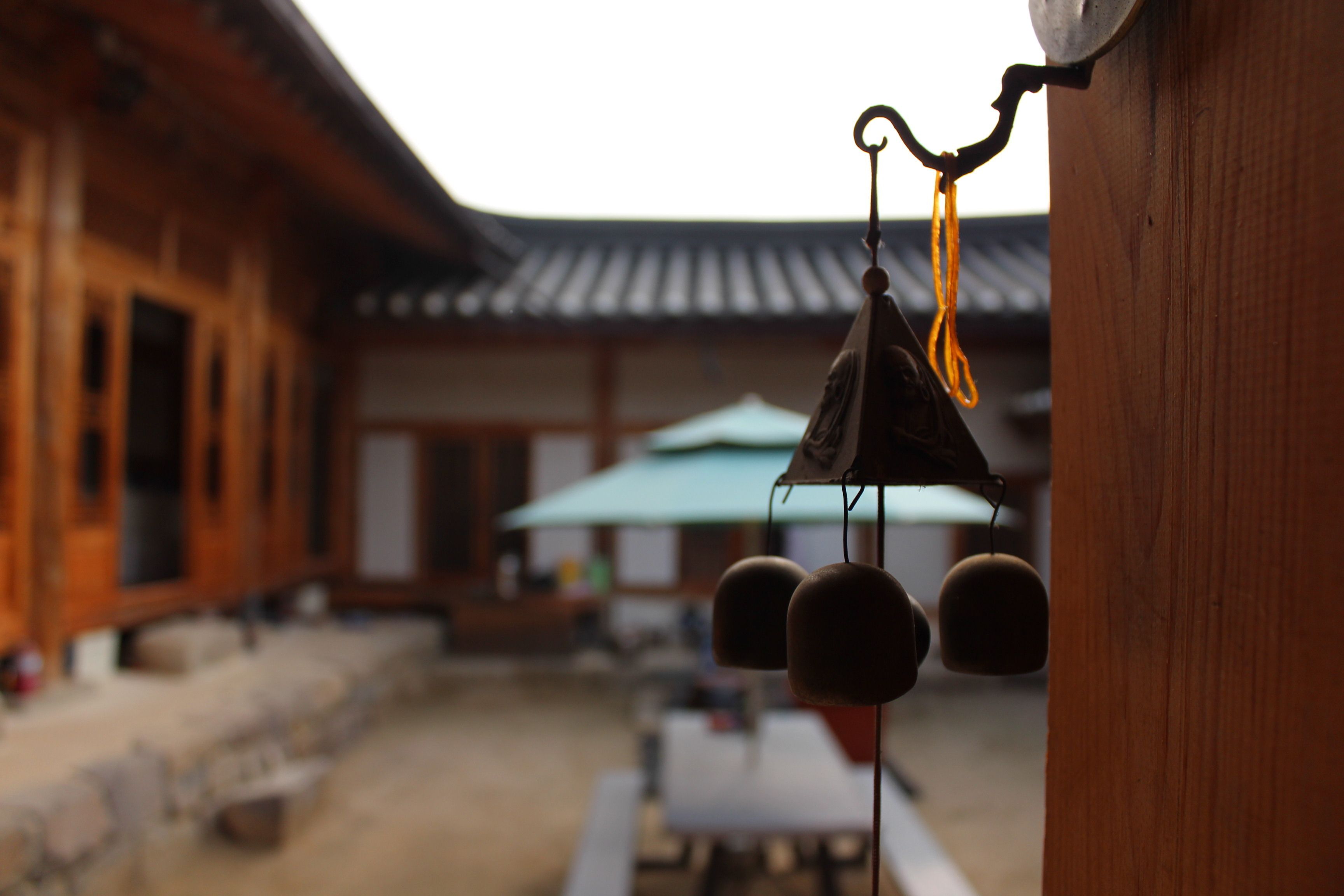 A traditional wooden building with a tiled roof, a hanging bell, and a table with a green umbrella in the background.