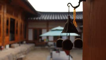 A traditional wooden building with a tiled roof, a hanging bell, and a table with a green umbrella in the background.
