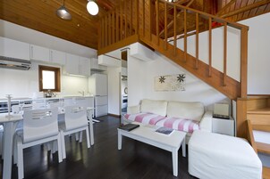 Una cocina moderna con armarios blancos, un comedor con sillas blancas y una escalera con barandilla de madera.