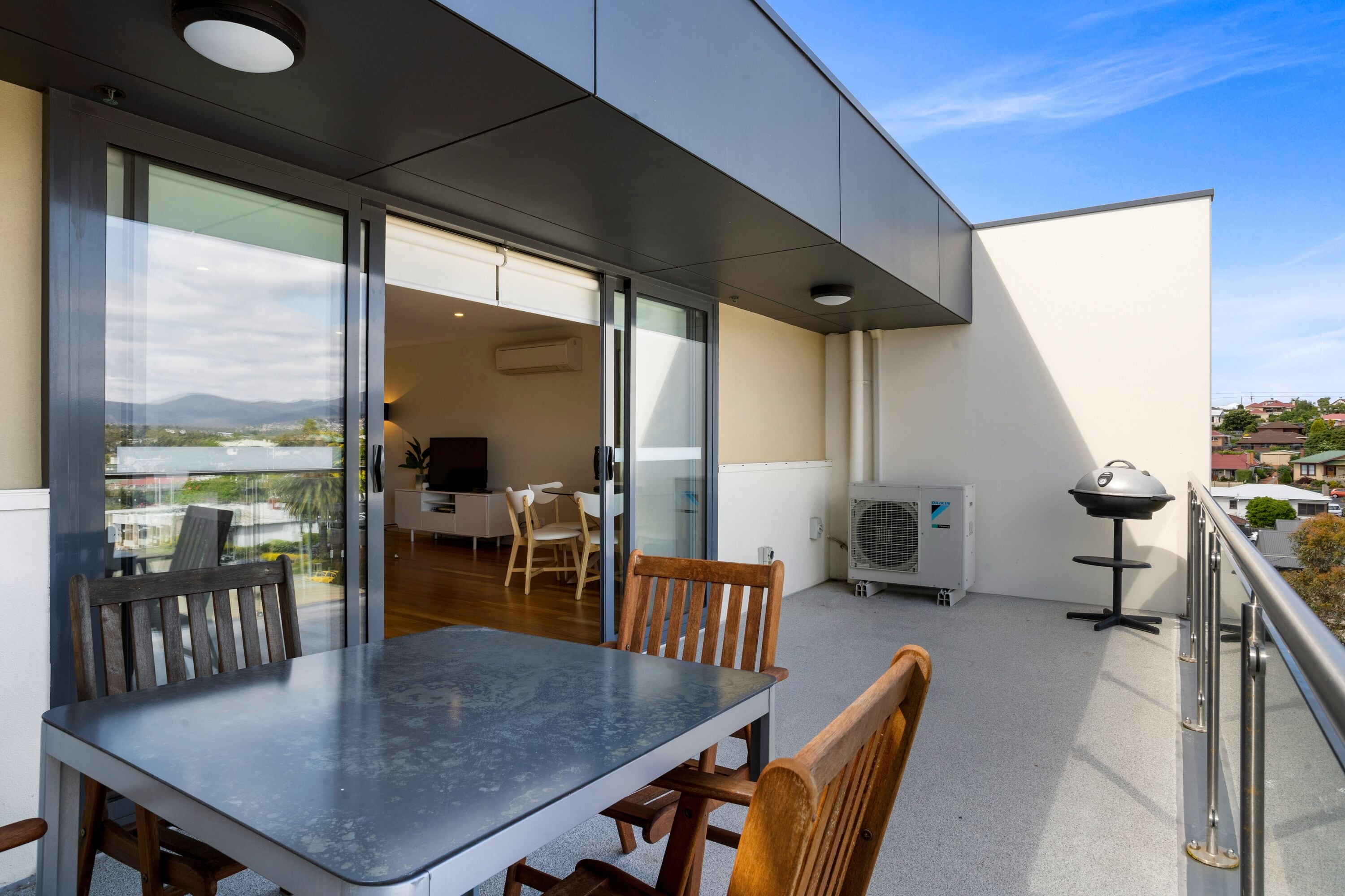 Een balkon met een tafel, stoelen, een barbecue en uitzicht op de stad.