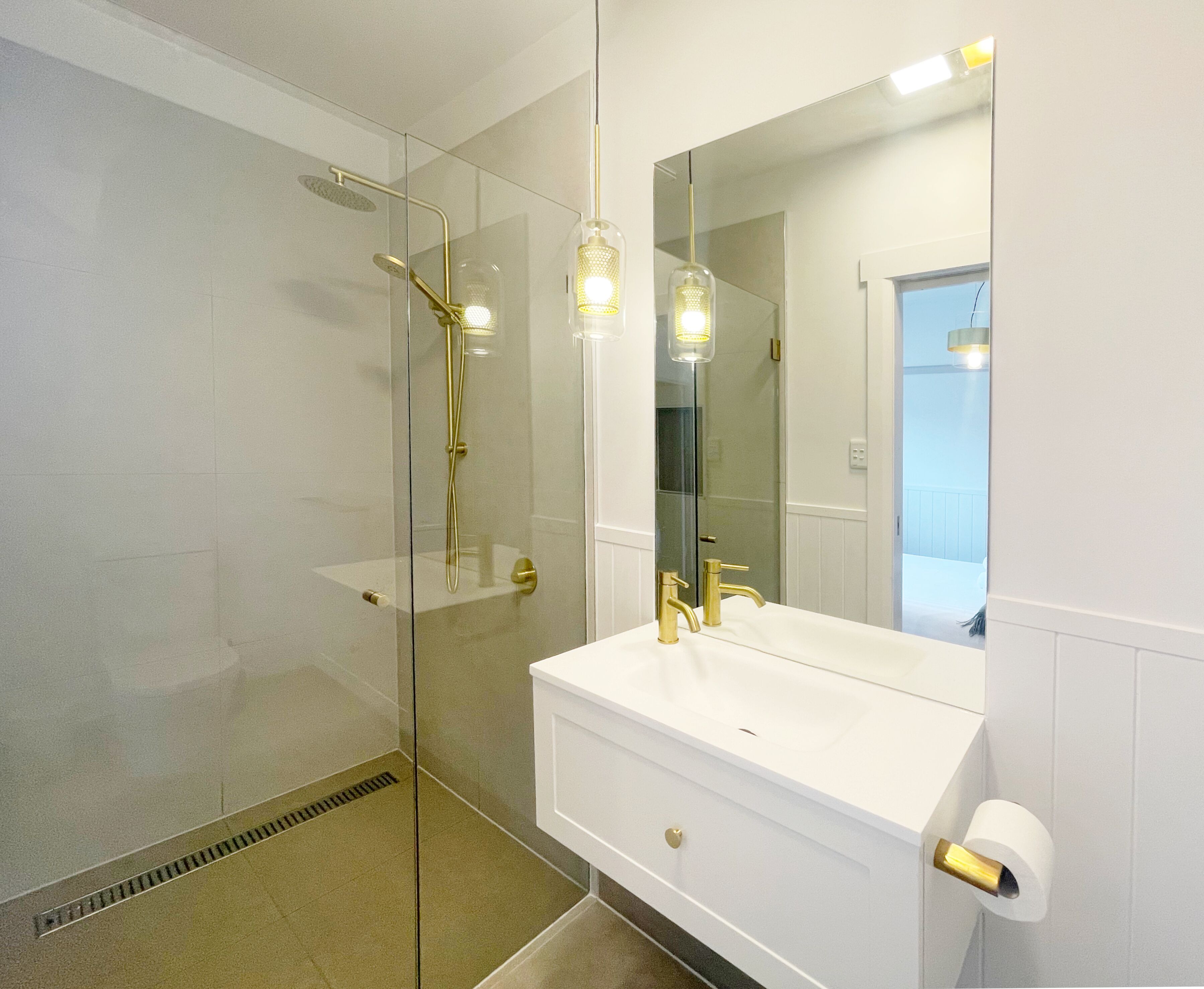 A modern bathroom with a glass-enclosed shower, a white vanity with gold fixtures, and a large mirror.
