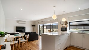 Una cocina moderna con una isla central, muebles blancos y un comedor con una mesa y sillas blancas.