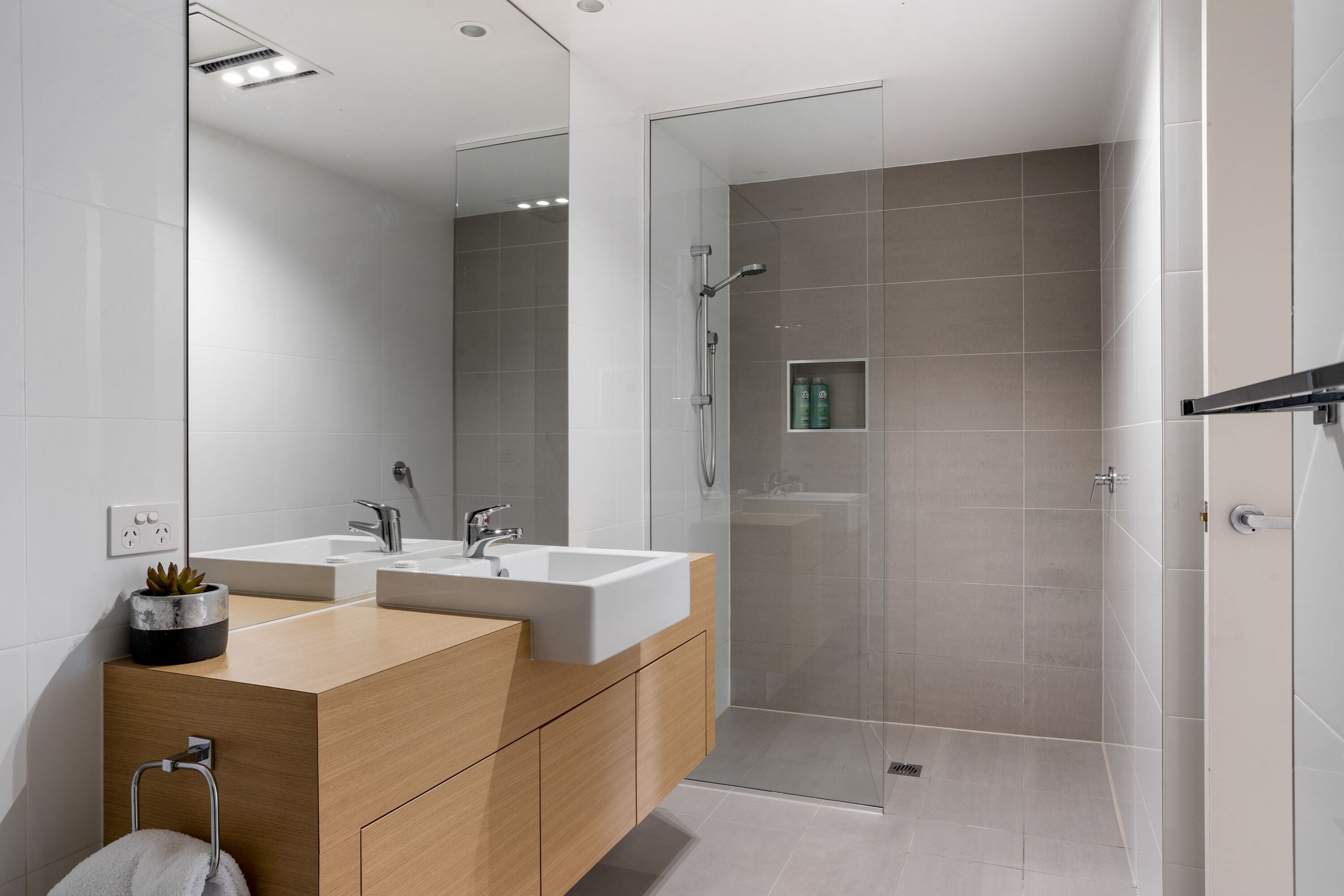 Un baño moderno con dos lavamanos, cabina de ducha de vidrio y tocador de madera.