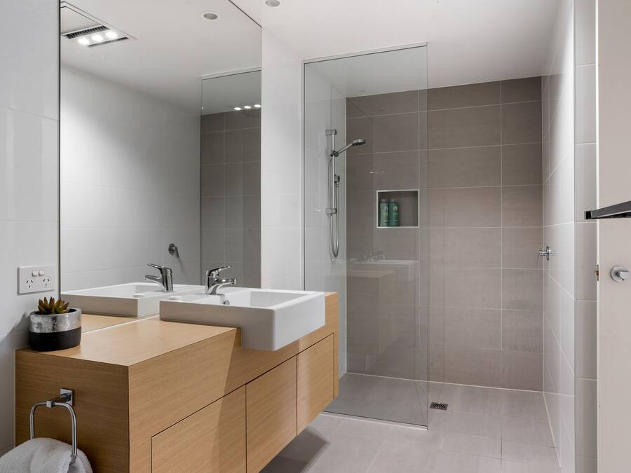 Un baño moderno con dos lavamanos, cabina de ducha de vidrio y tocador de madera.
