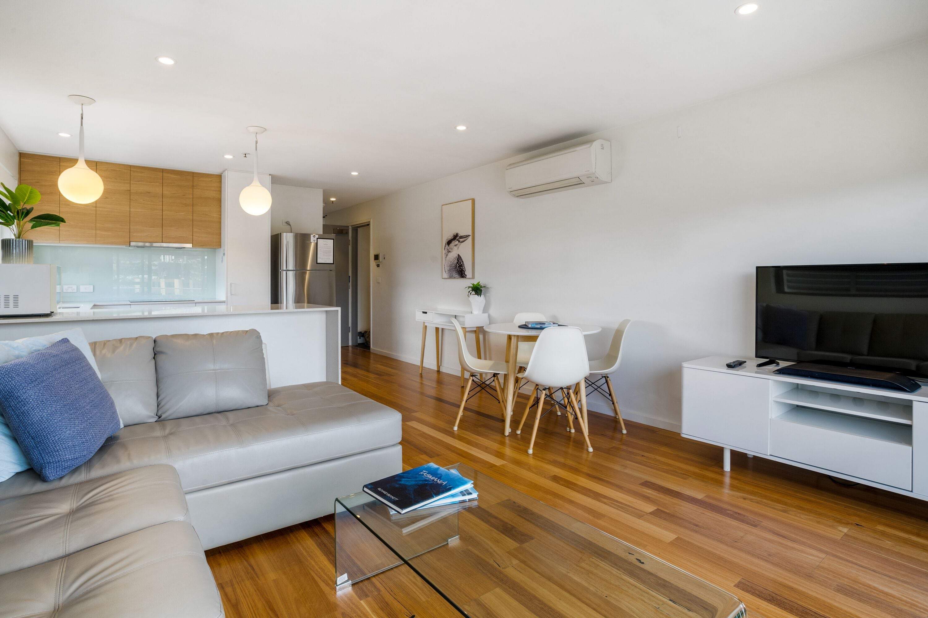 Una sala de estar moderna con sofá, mesa de centro, mueble para televisión y zona de comedor.