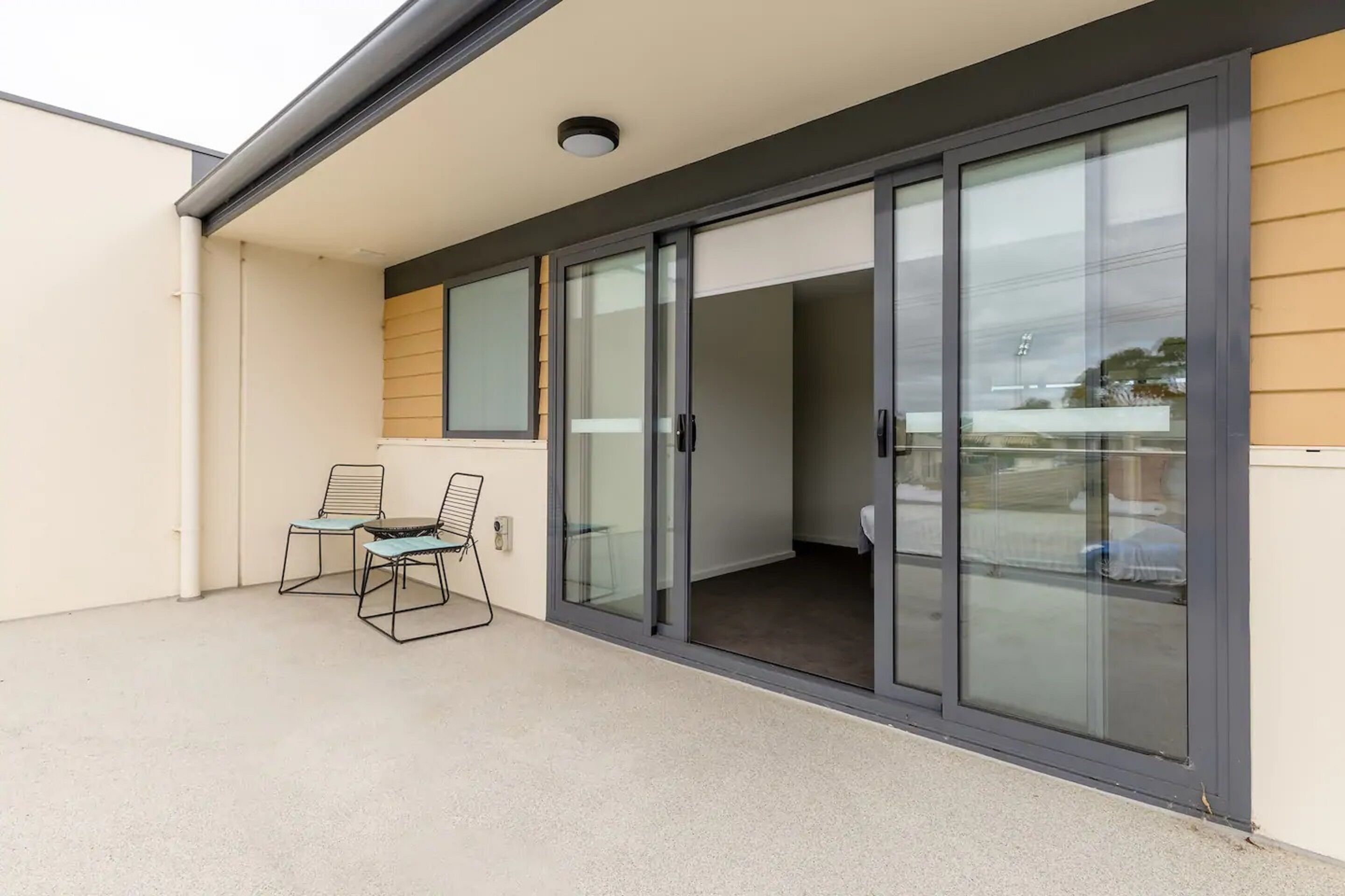 A balcony with two chairs and a table, a sliding glass door, and a view of the street.