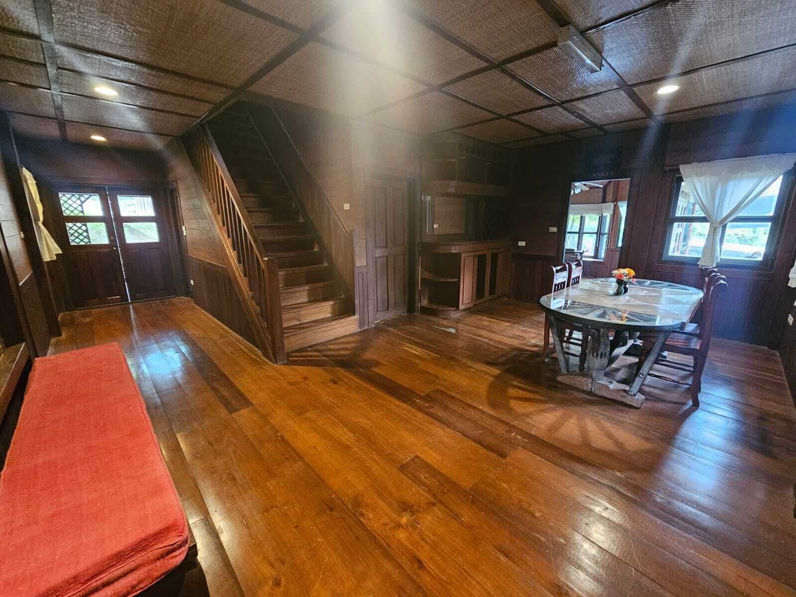 Una habitación amplia con pisos de madera, una escalera, un comedor con mesa y sillas, y un ventanal con cortinas.