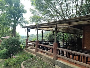 Un espacio de descanso al aire libre con detalles rústicos, madera, mesas y abundante vegetación.