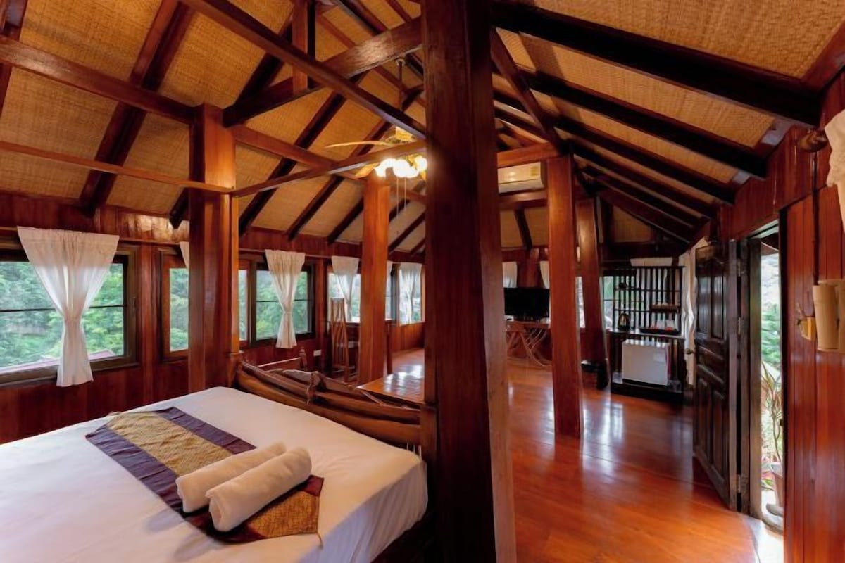 A spacious room with a large bed, wooden beams, and a view of the outdoors.