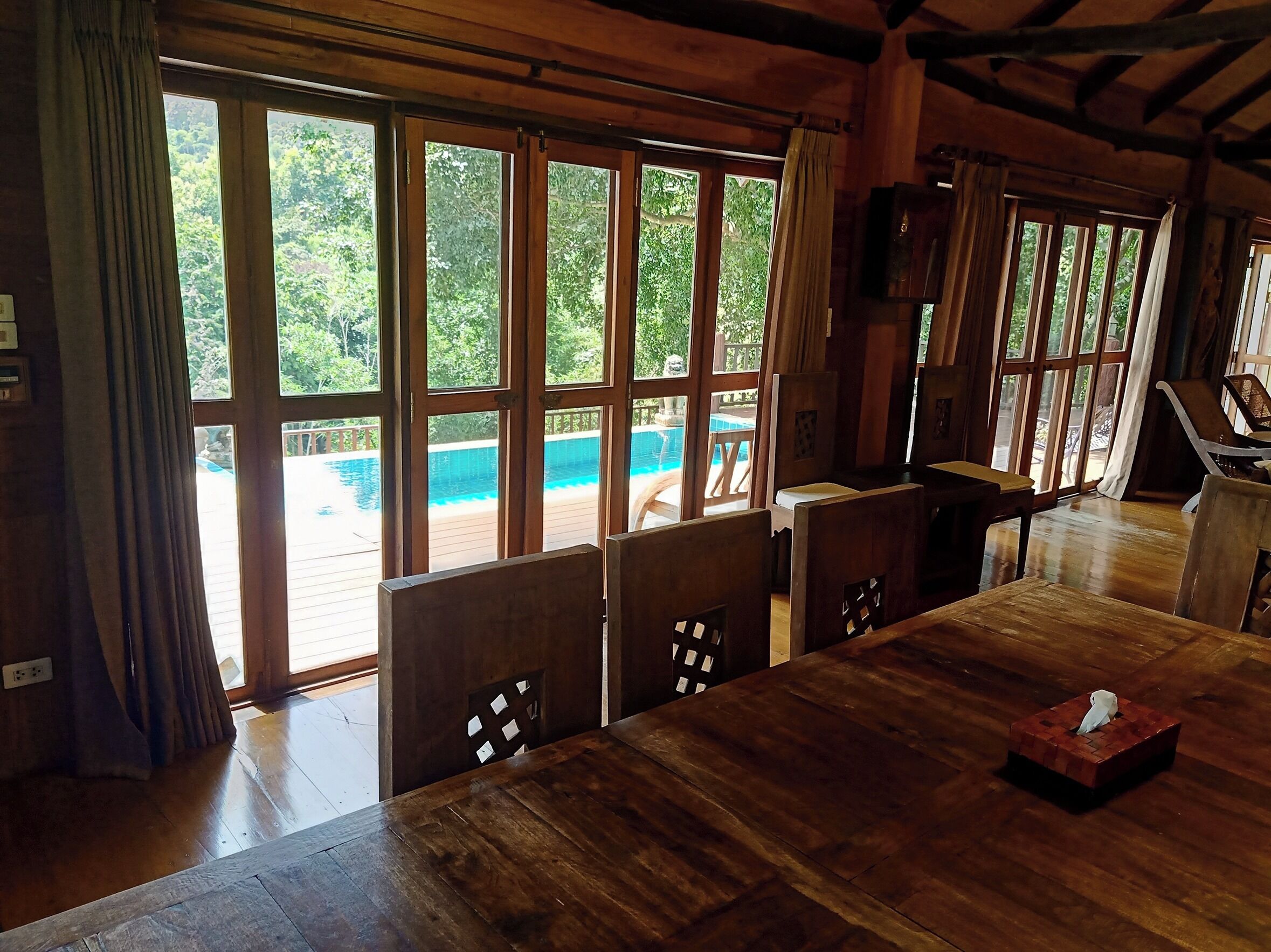A wooden dining area with large windows overlooking a pool.