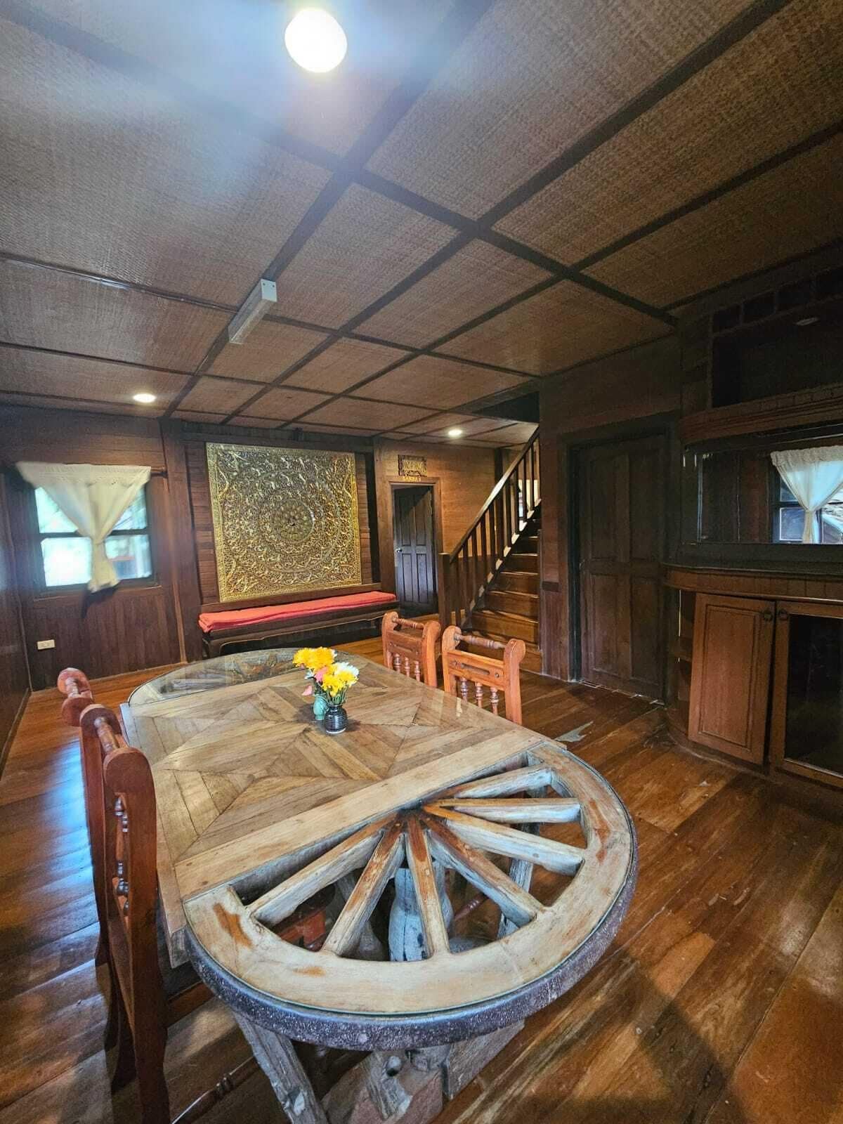 Un comedor rústico con una gran mesa de madera, sillas y un adorno central con una rueda decorativa.